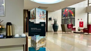 Un espace d’accueil d’hôtel comprenant un coin café, une grande affiche représentant un couple, un fauteuil rouge et un tableau de perroquets.