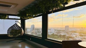 Une pièce dotée de grandes fenêtres, d’un fauteuil suspendu et offrant une vue sur le paysage urbain au coucher du soleil.