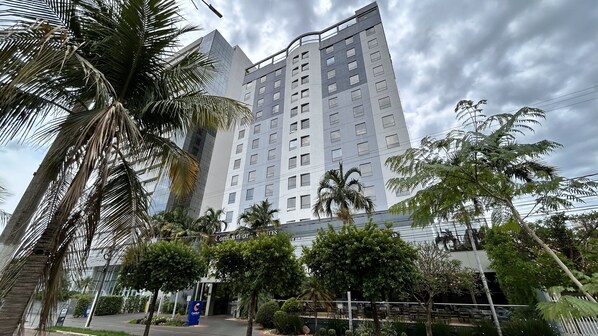 Um hotel moderno e alto, com vários andares, cercado por palmeiras e vegetação.