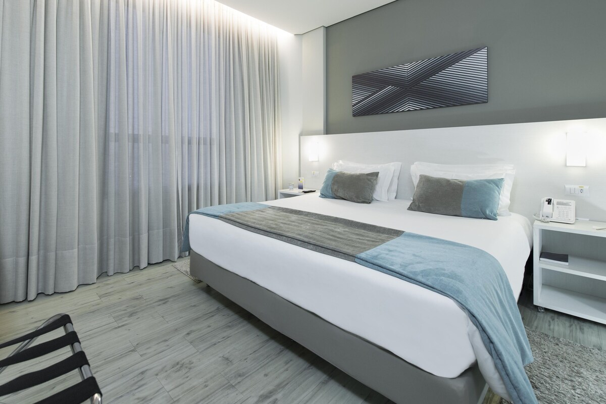 A modern hotel room with a large bed, bedside tables, a desk, and a chair.