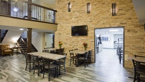 A spacious indoor area with a high ceiling, a staircase, and a flat-screen TV mounted on a brick wall.