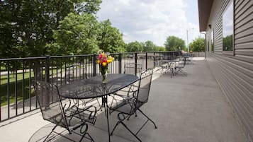 A patio with a round table and chairs, a vase of flowers, and a view of trees and a building.