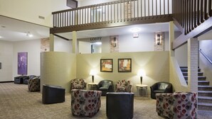 A lobby with a staircase, seating area with patterned chairs and ottomans, and a 'Lobby' sign.
