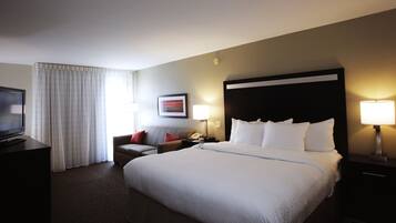 A hotel room with a large bed, a TV, a desk, a chair, and a sofa.