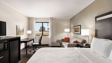 A hotel room with a large bed, a desk, a chair, a sofa, and a television.