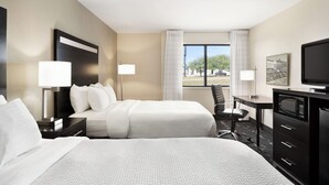 A hotel room with two beds, a desk, a television, and a view of the outdoors.