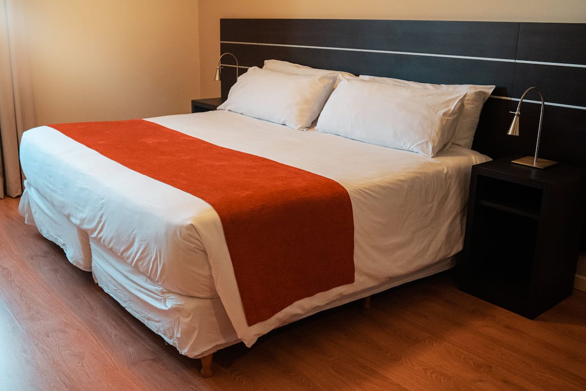 A neatly made bed with white and orange bedding, a wooden headboard, and a nightstand with a lamp.
