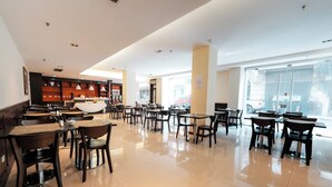 Un'ampia sala ristorante con numerosi tavoli e sedie, una zona cucina e ampie finestre che lasciano entrare la luce naturale.