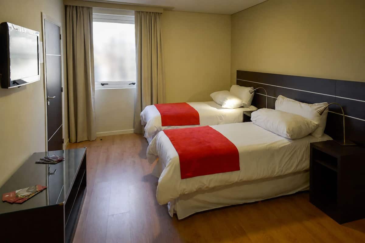 A hotel room with two beds, a TV, a desk, and a window with curtains.