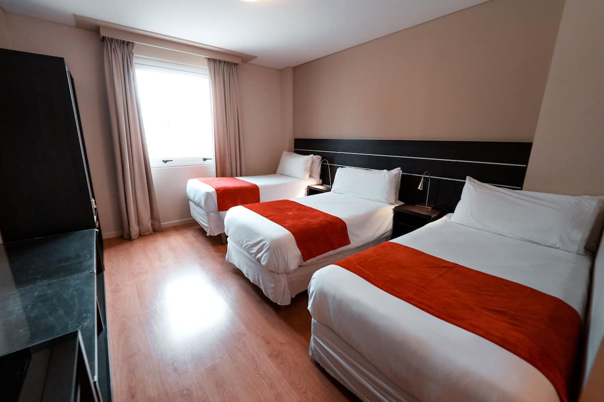 A hotel room with two beds, a desk, and a window with curtains.