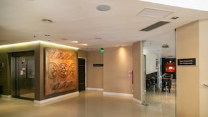 Un'accogliente hall di un hotel moderno, con un'ampia parete decorata da un murale, una reception e una scalinata che conduce ai piani superiori.