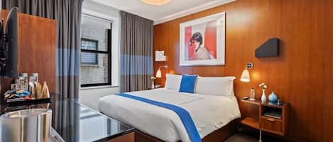 A hotel room with a bed, bedside table, lamp, and a view of the outside.