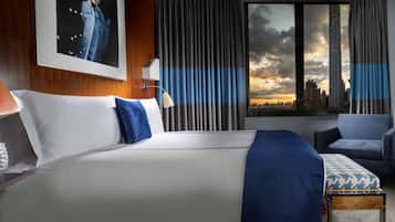 Habitación de hotel con una cama grande, vista del horizonte urbano y paisaje citadino visible a través de la ventana.
