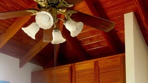 Una habitación con ventilador de techo de madera, un armario grande de madera y una silla estampada.