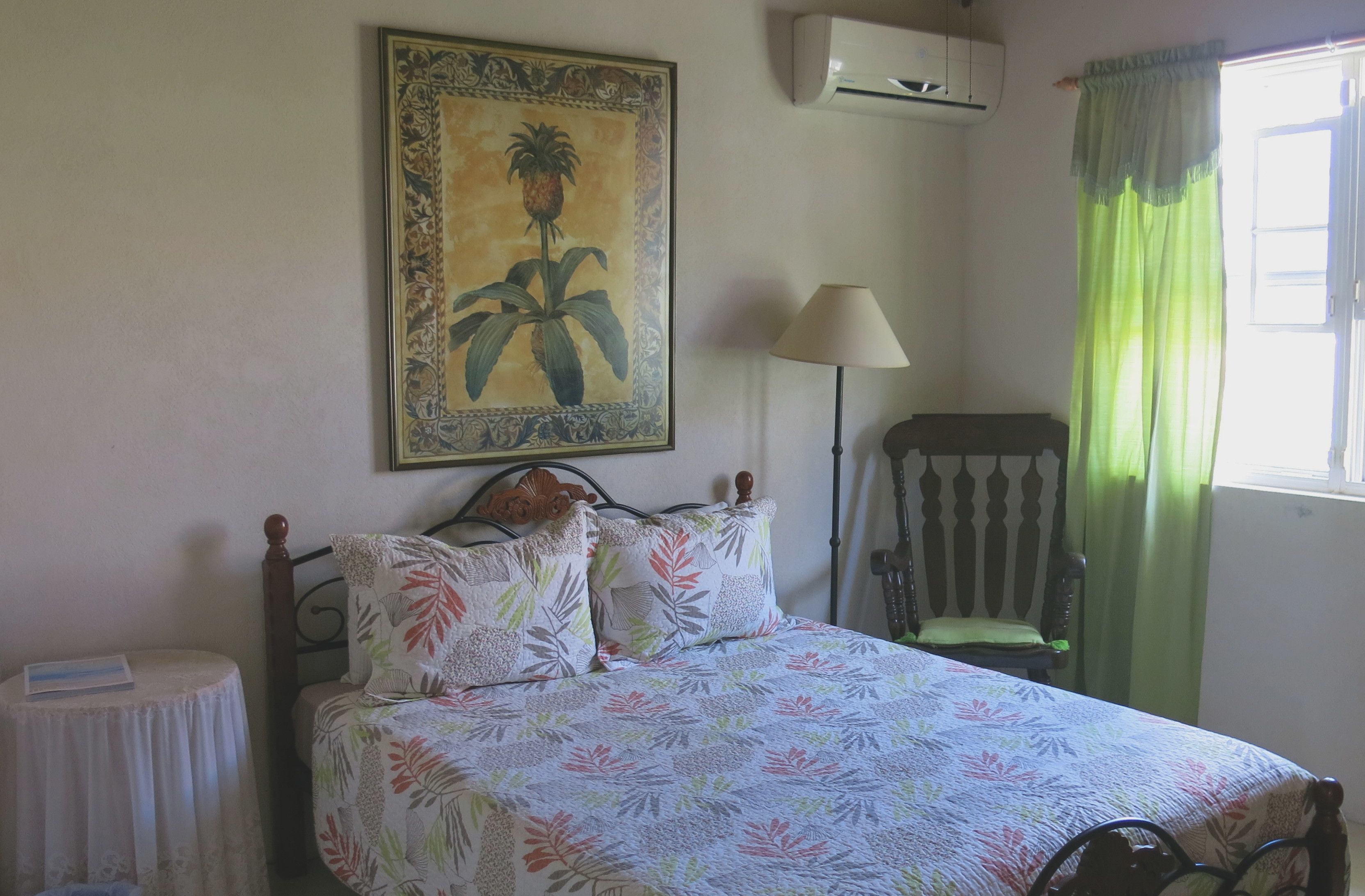 A bedroom with a bed, a chair, a table, a painting, and a window with curtains.