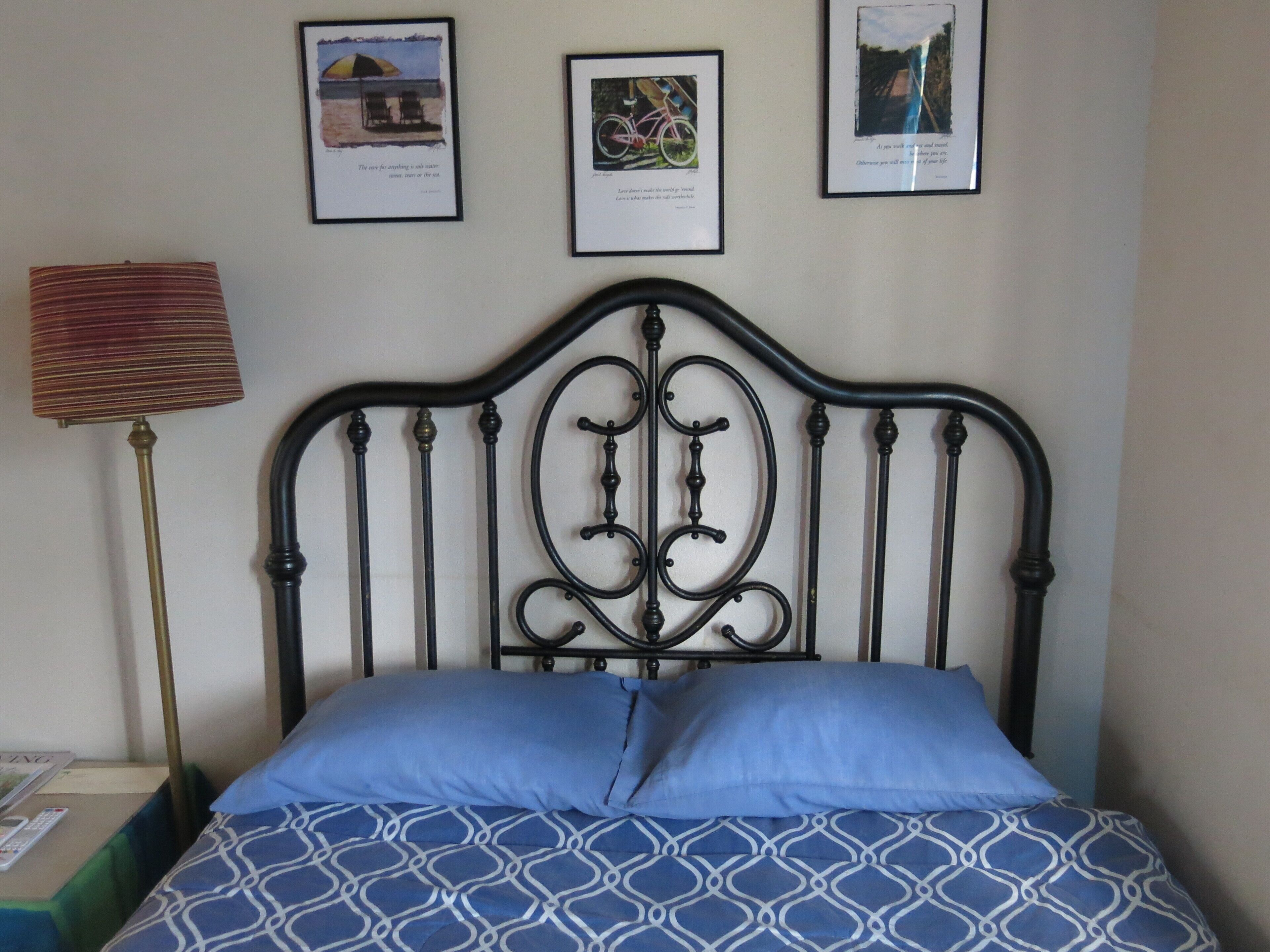 Una camera da letto con testiera in metallo, un letto con copriletto a motivi blu e tre quadri appesi al muro.