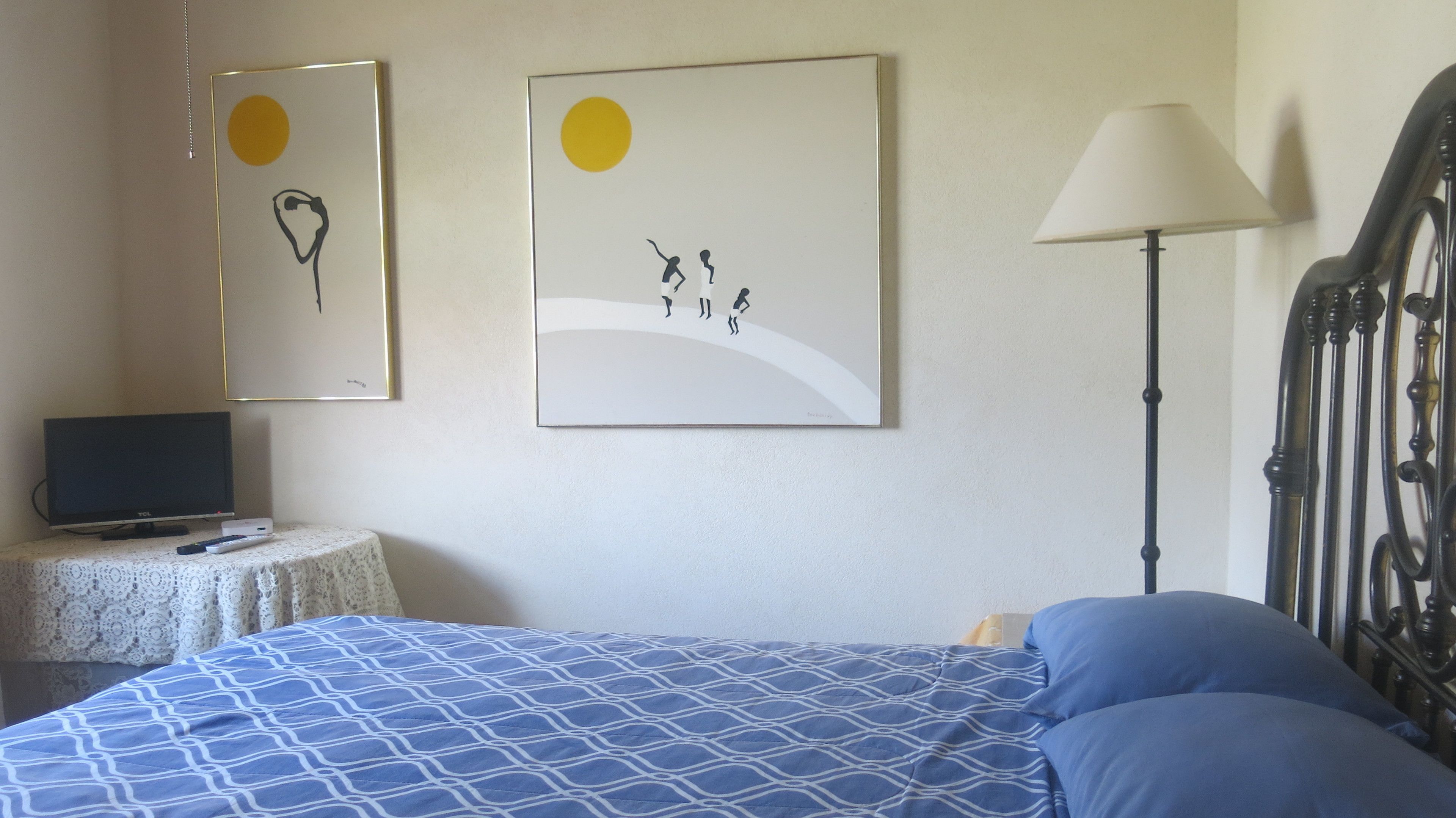 A bedroom with a bed, a TV on a side table, and two wall-mounted artworks.