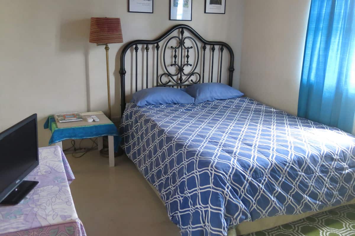 Um quarto com uma cama, uma escrivaninha com um computador, uma luminária e três quadros na parede.