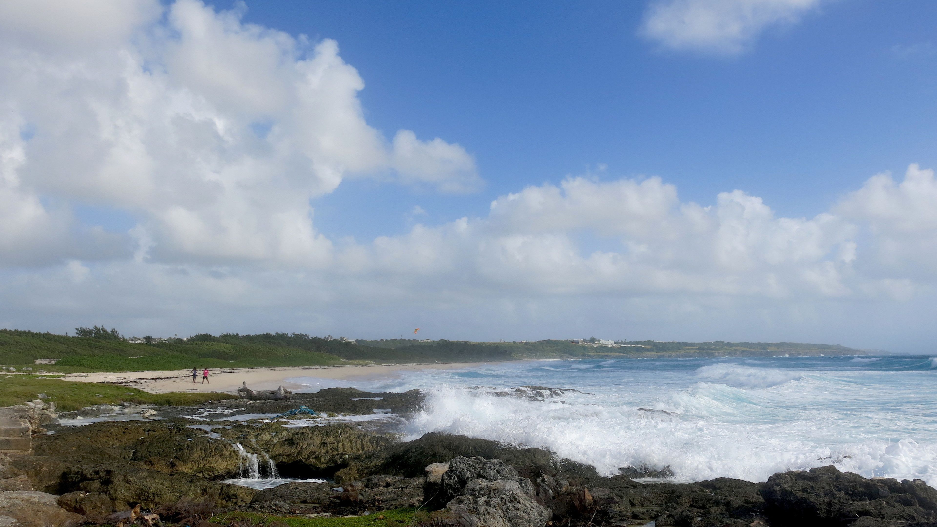 A coastal landscape with rocky shores, waves crashing onto the beach, and a clear sky.
