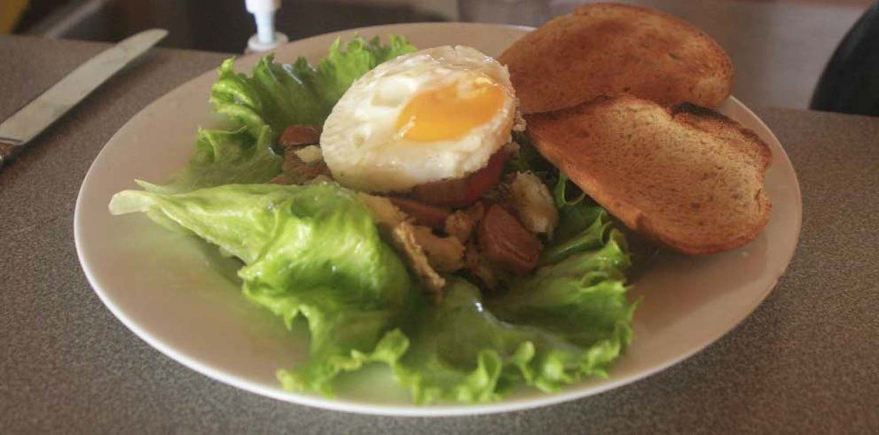 Un plato con ensalada, un huevo frito y dos rebanadas de tostada.