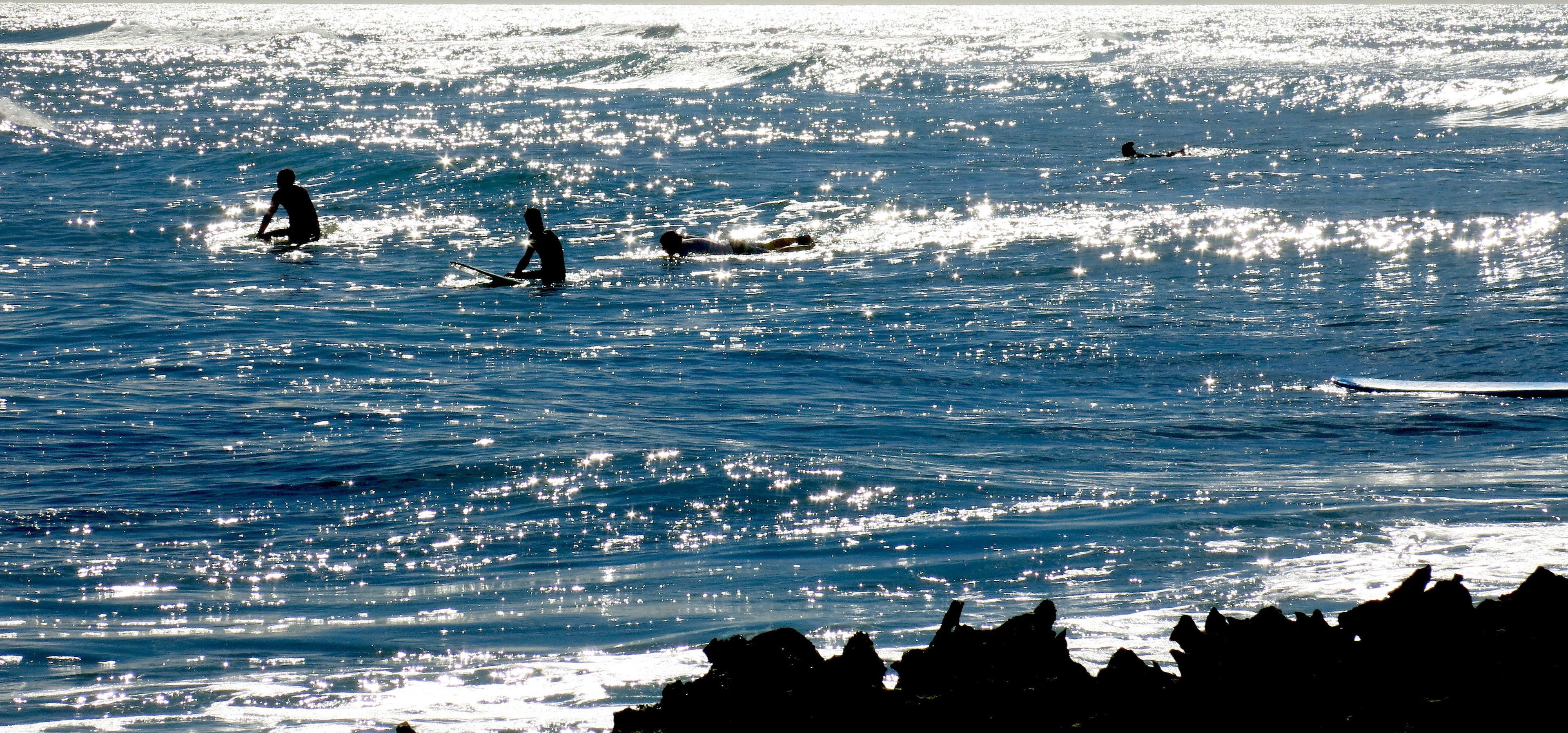 Een strand met surfers in het water en rotsen op de voorgrond.