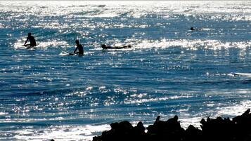 Een strand met surfers in het water en rotsen op de voorgrond.