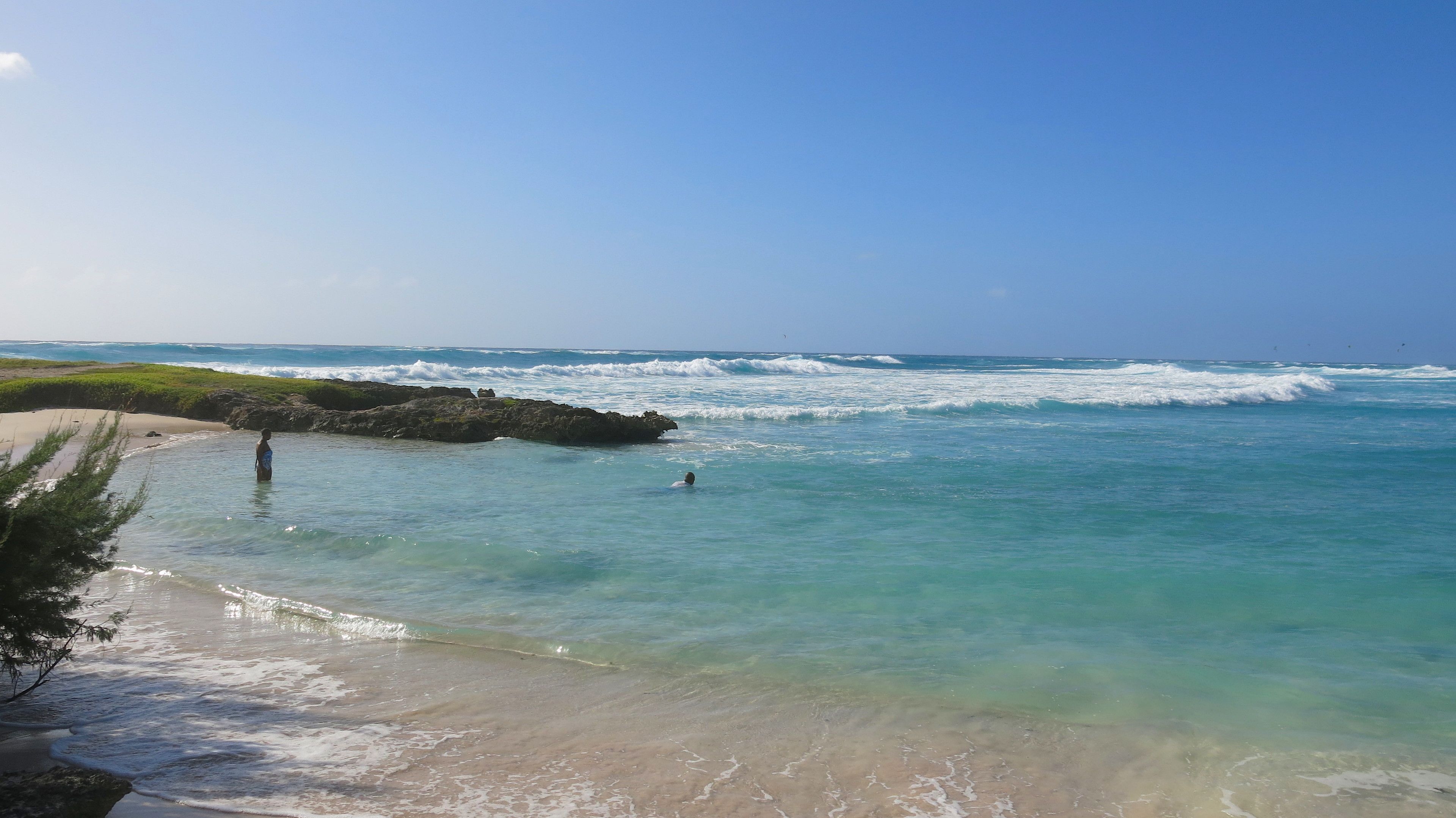 Una playa con agua turquesa cristalina, una orilla arenosa y afloramientos rocosos.