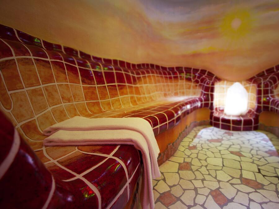 Un cuarto de spa con piso de mosaico, un banco y una toalla.