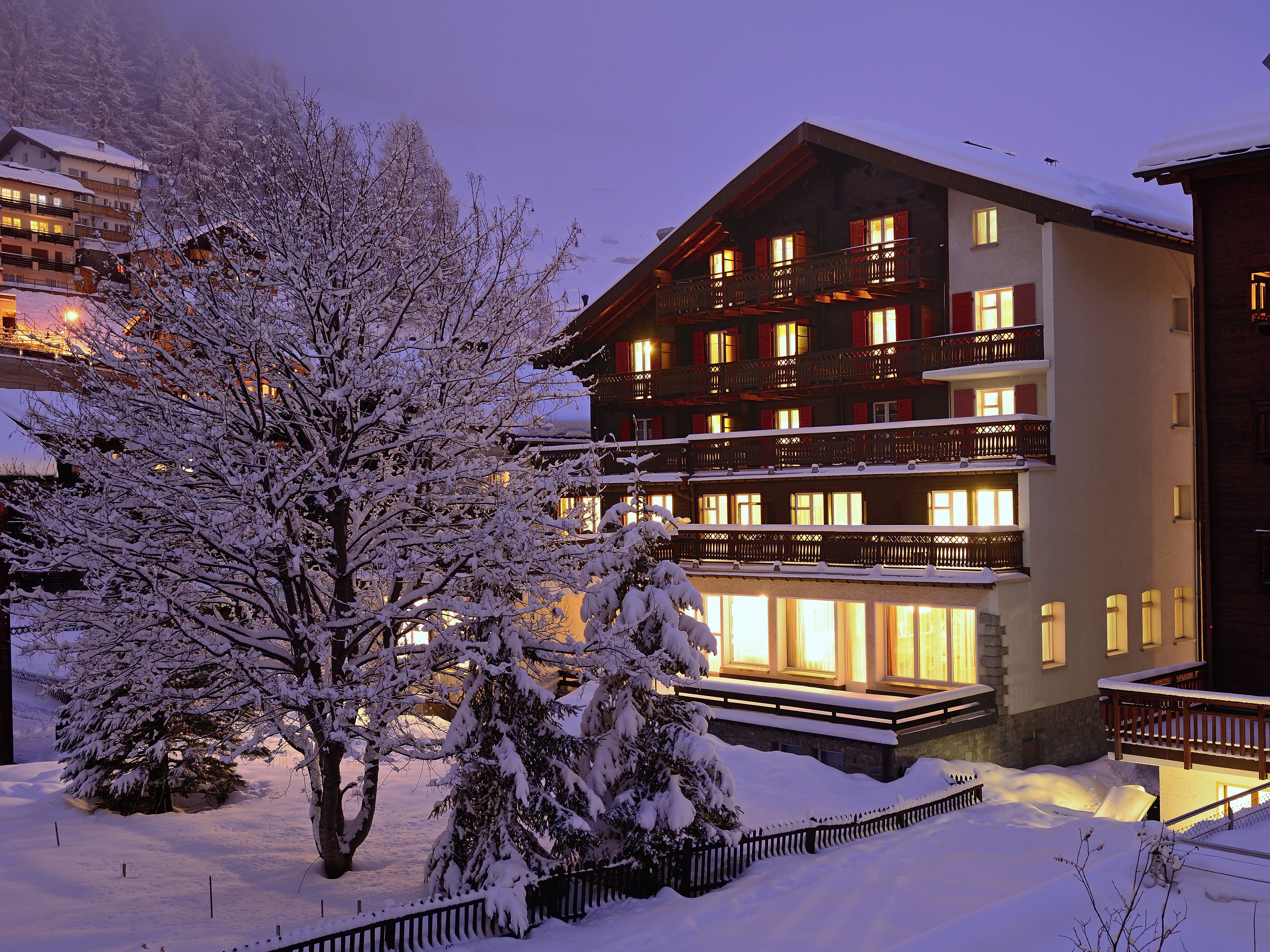 Um hotel com vários andares, varandas, árvores cobertas de neve e fachada bem iluminada.