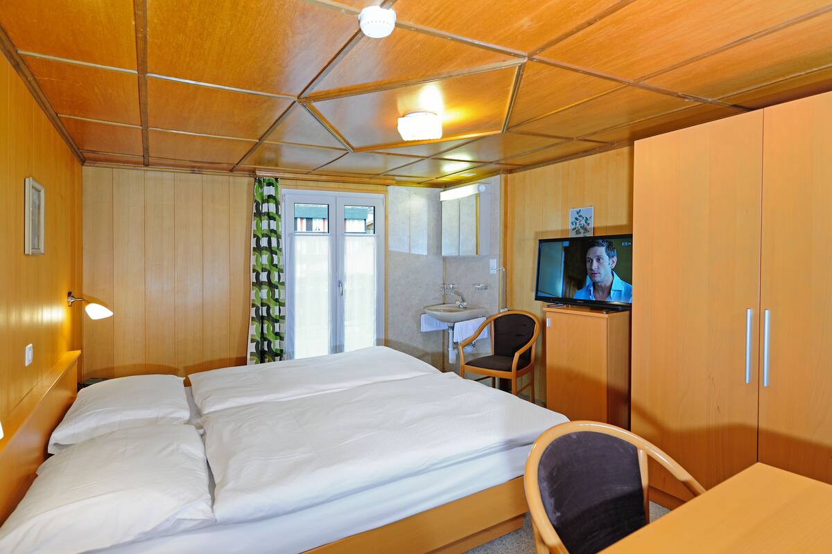 Ein Hotelzimmer mit Bett, Schreibtisch, Stuhl, Fernseher und einem Badezimmer mit Waschbecken und Spiegel.
