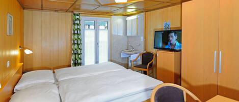 A hotel room with a bed, a desk, a chair, a television, and a bathroom with a sink and mirror.