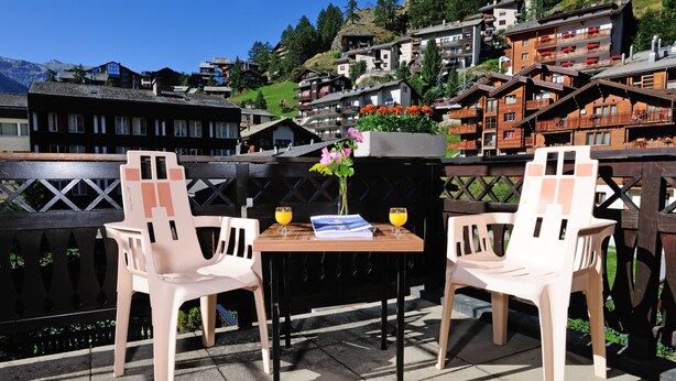 Una terraza con dos sillas de plástico blanco, una mesa de madera y un florero con flores.
