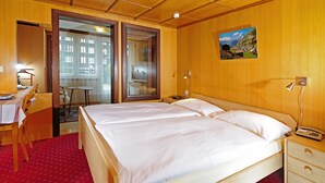 Habitación de hotel con una cama grande, un escritorio con silla, una mesita y un cuadro en la pared.
