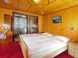 Habitación de hotel con una cama grande, un escritorio con silla, una mesita y un cuadro en la pared.