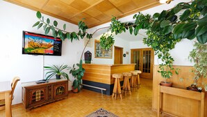 Un vestíbulo acogedor con un mostrador de recepción de madera, taburetes de bar, un televisor montado en la pared y varias plantas en macetas.