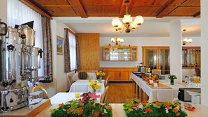 Un comedor con techo de madera, una cafetera, mesas con centros de flores y una cocina al fondo.