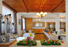 Un comedor con techo de madera, una cafetera, mesas con centros de flores y una cocina al fondo.