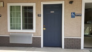 A building with a blue door, a window with curtains, and a sign indicating an accessible office. - Pacific Motel (Gridley)