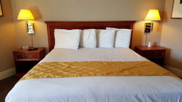 A hotel room with a large bed, two bedside tables, and two wall-mounted lamps. - Pacific Motel (Gridley)