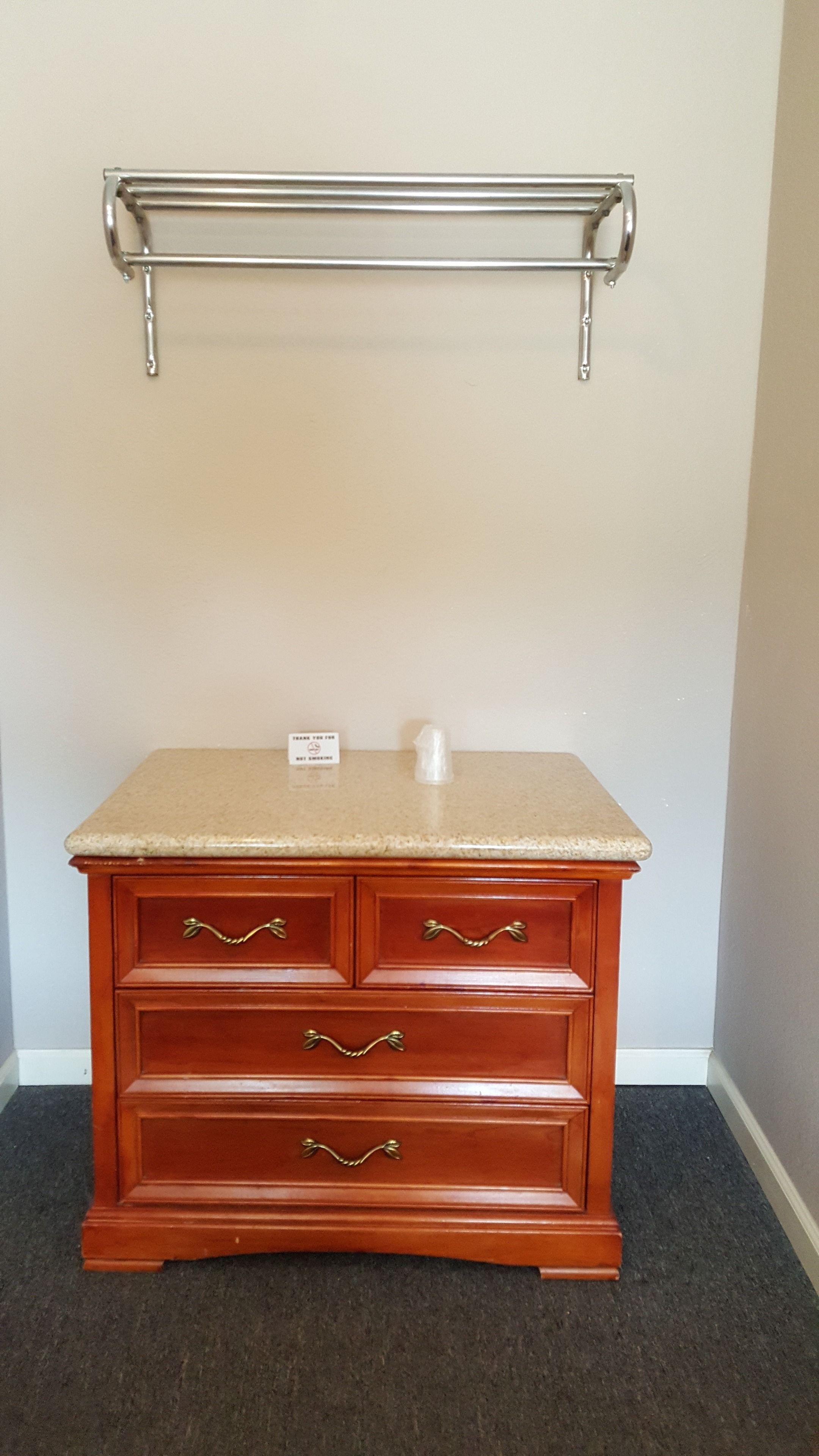A wooden dresser with drawers and a countertop, a metal shelf above it, and a small sign on the countertop.