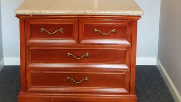 A wooden dresser with drawers and a countertop, a metal shelf above it, and a small sign on the countertop.