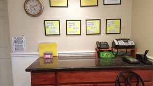 A hotel reception desk with framed weekly specials signs, a clock, a pet fee sign, and a cash deposit box. - Pacific Motel (Gridley)