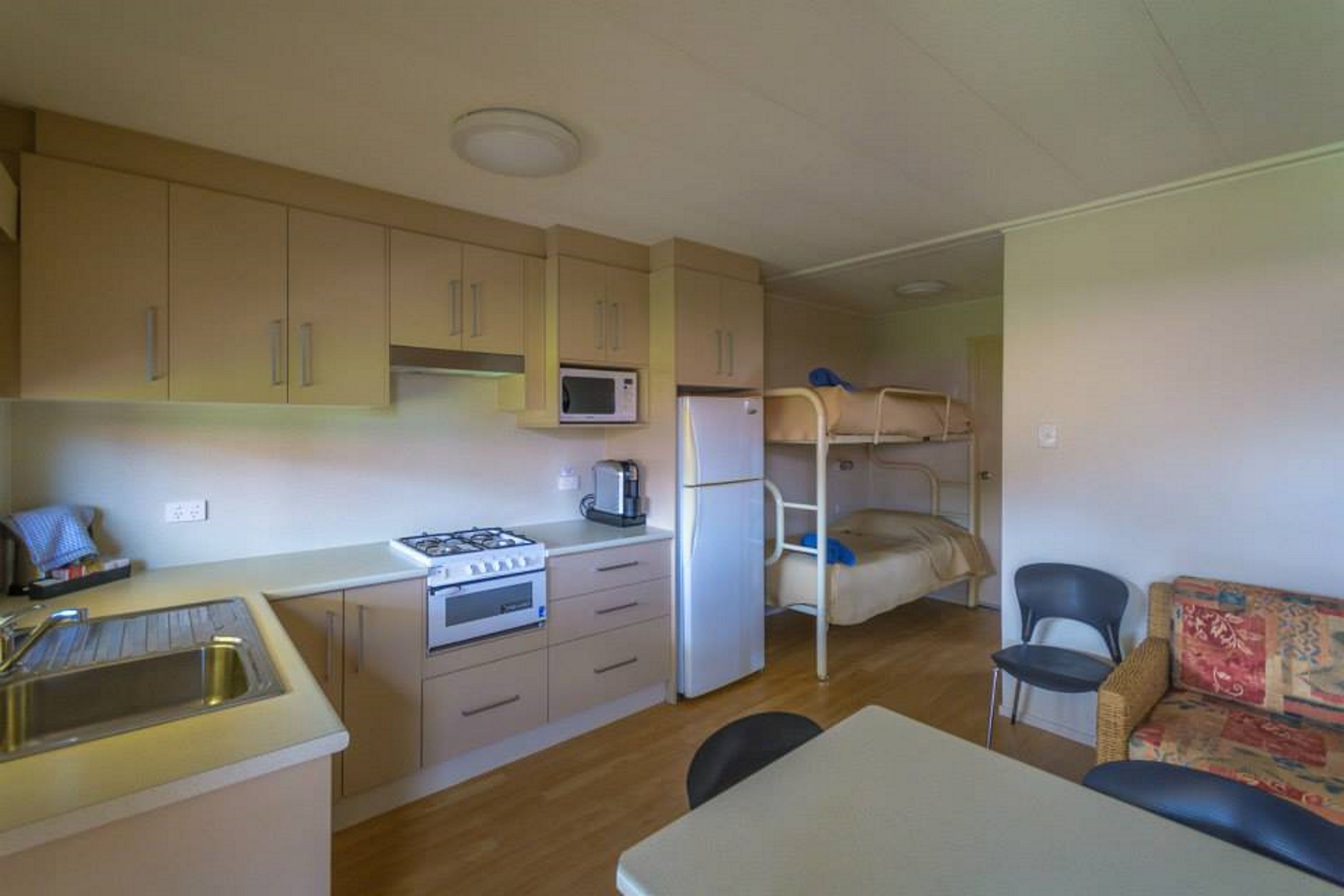 A compact kitchen with a gas stove, microwave, and refrigerator, a bunk bed, and a small dining area with a table and chairs.