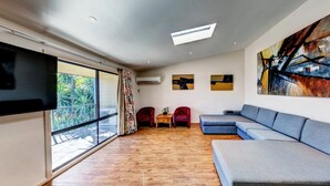 A modern living room with a large grey sectional sofa, a flat-screen TV mounted on the wall, and a large abstract painting.