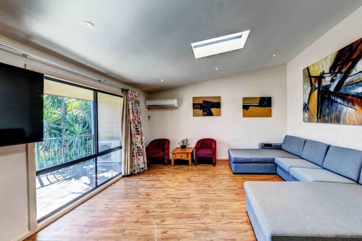 A modern living room with a large grey sectional sofa, a flat-screen TV mounted on the wall, and a large abstract painting.