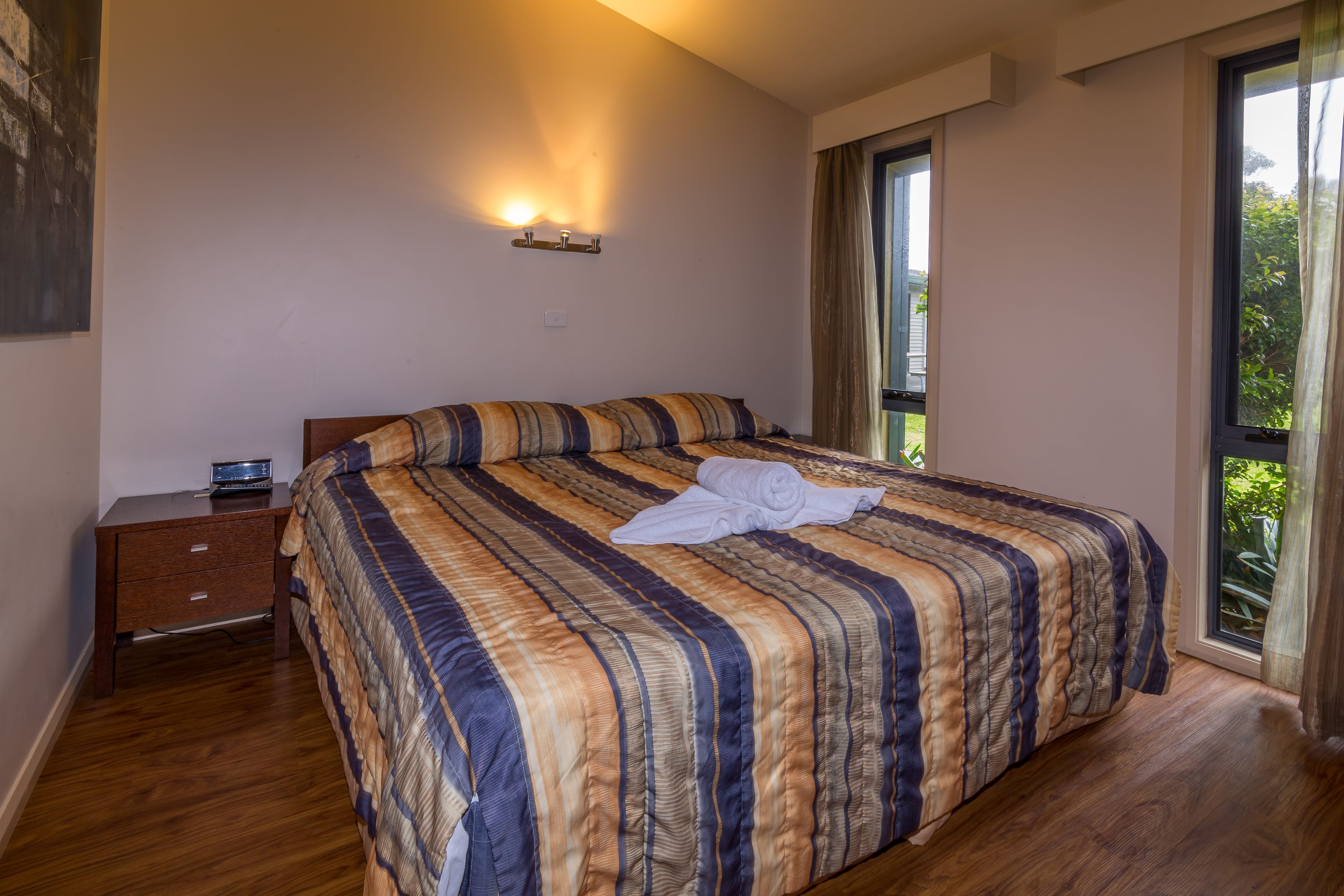 Um quarto com uma cama grande, uma mesa de cabeceira, uma luminária na parede e uma janela com cortinas.
