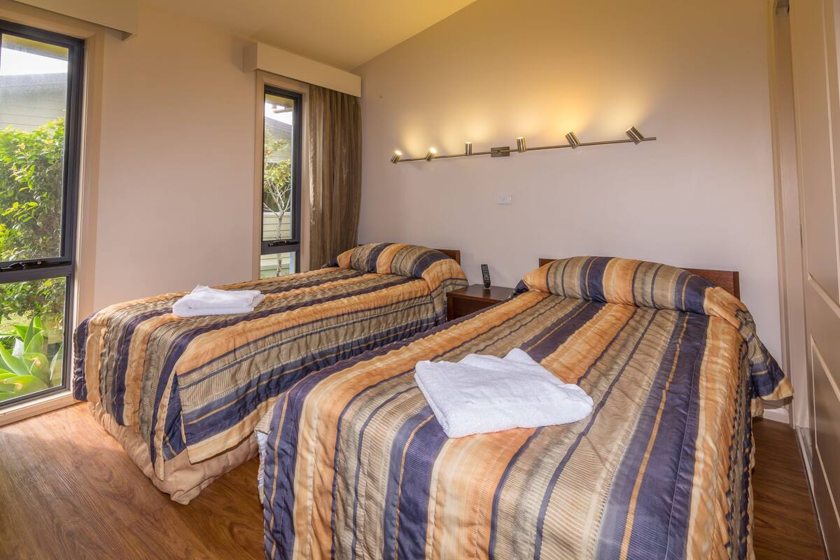 A hotel room with two beds, a window, and a wall-mounted light fixture.