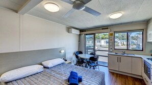 A hotel room with a bed, a desk, a chair, a kitchenette, and a window with a view of the outside.