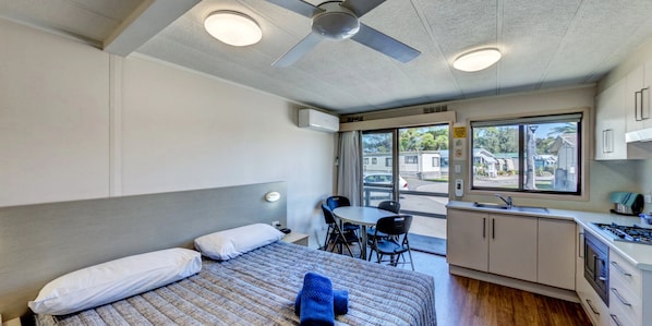 Habitación de hotel con cama, escritorio, silla, kitchenette y ventana con vistas al exterior.