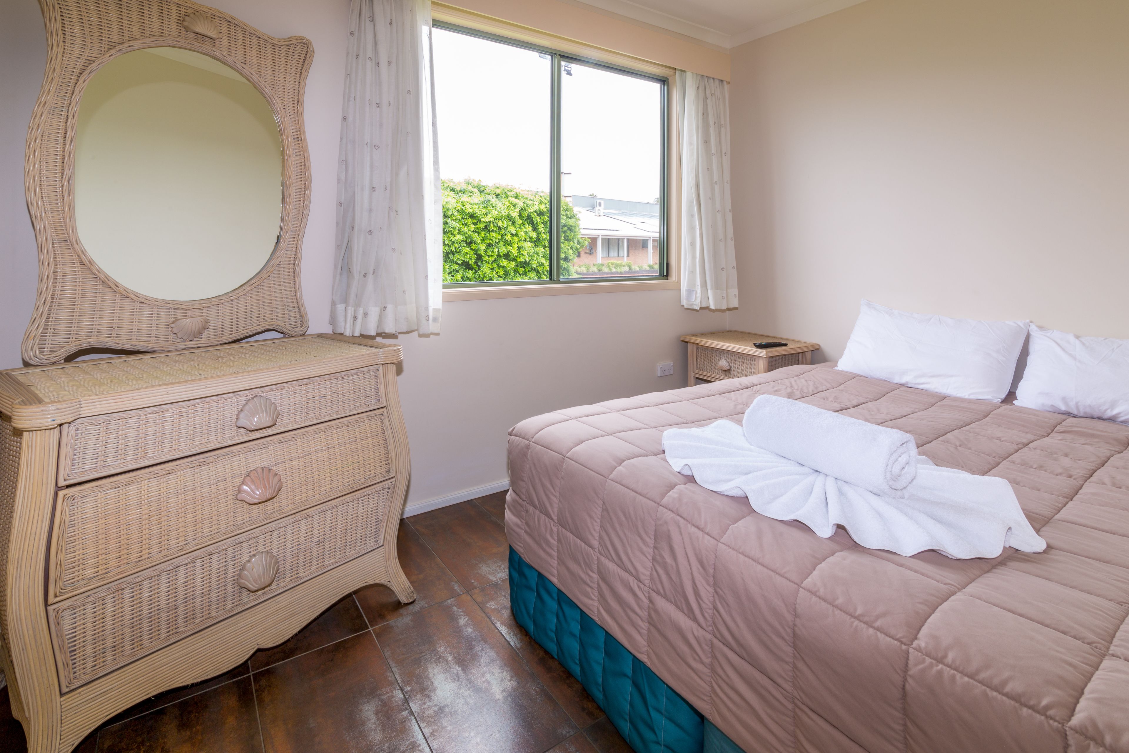 Een slaapkamer met een bed, een dressoir, een spiegel en een raam met gordijnen.